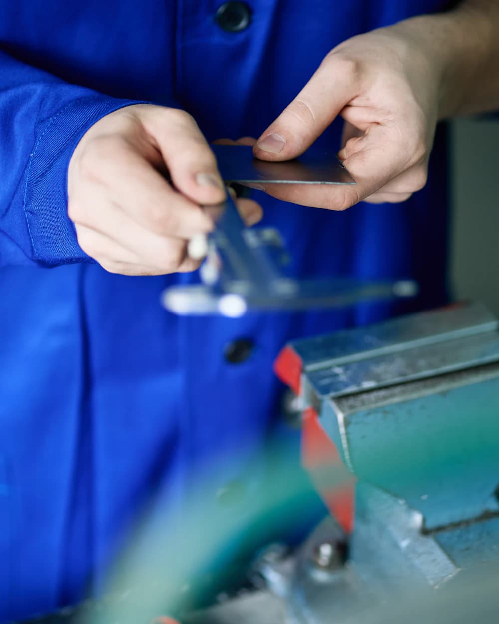 A worker's hands in blue overalls measuring a metal part with a caliper.